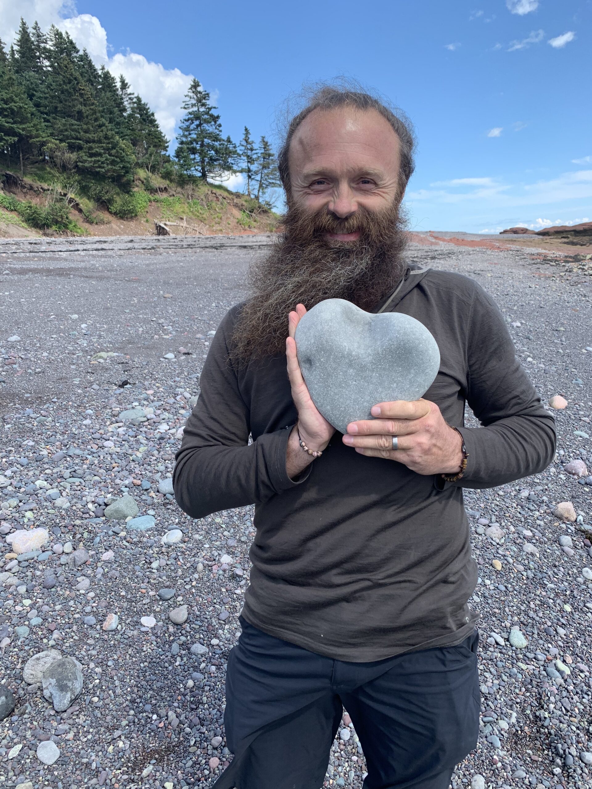 Men holding a heart-shaped stone on a pebble beach