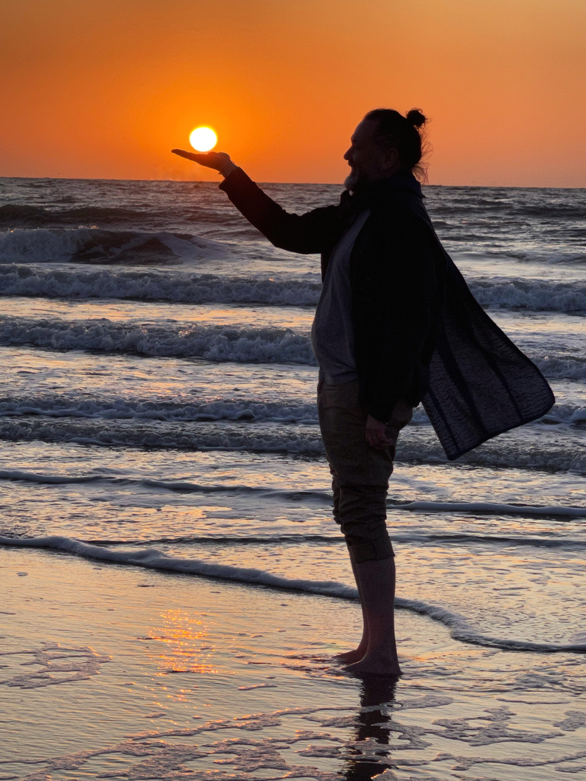 Men at the seaside holding the sun in his hand, at sunset